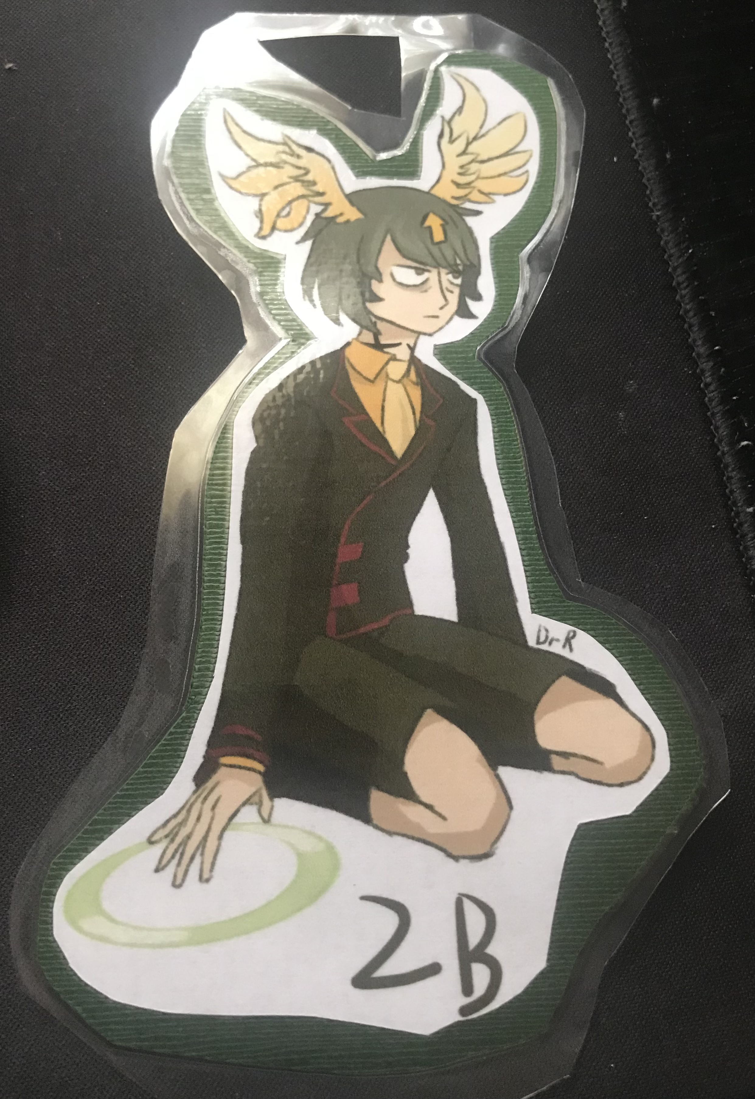 a badge of Delilah dressed like Noah from Daemon bride. They are crouched down while '2B' is beneath them